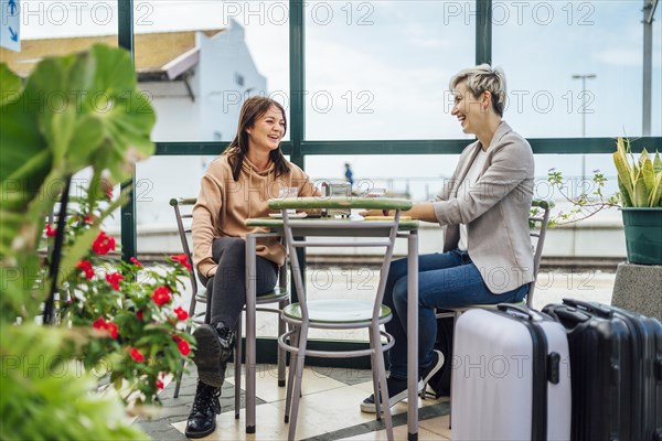 Two travelling women with luggage drinking coffee at train station