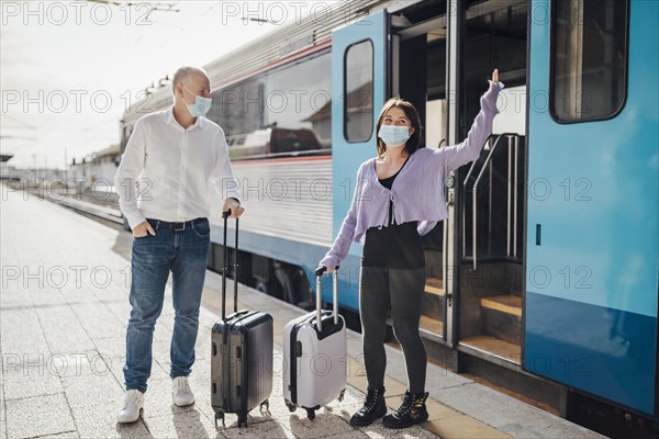 Tourists with suitcases and masks on the platform next to the train