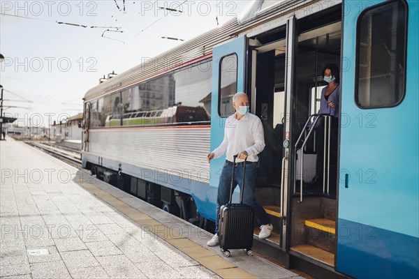 Tourists with suitcases and masks on exiting the train