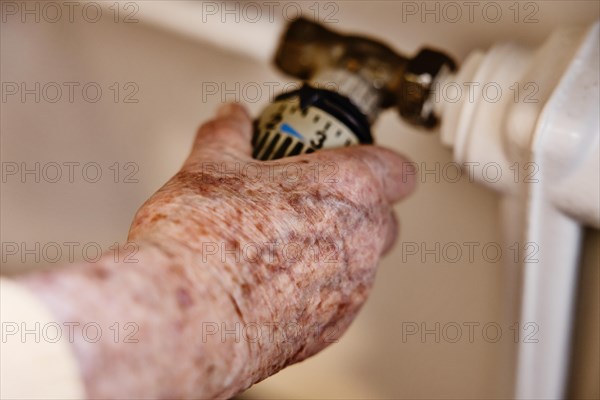 Hand of a senior citizen with age spots on the thermostat of a heater