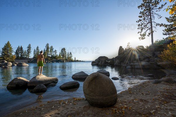 Young man in swimming trunks standing on a round stone in the water