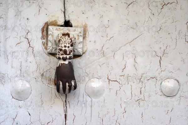 Iron door knocker as hand on white wooden door