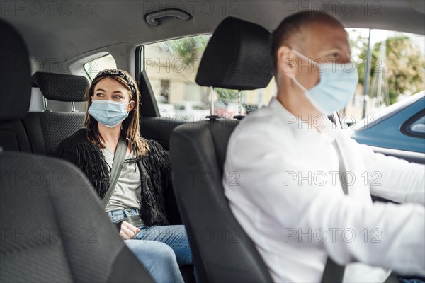 Taxi driver in a mask with a female client on the back seat wearing mask