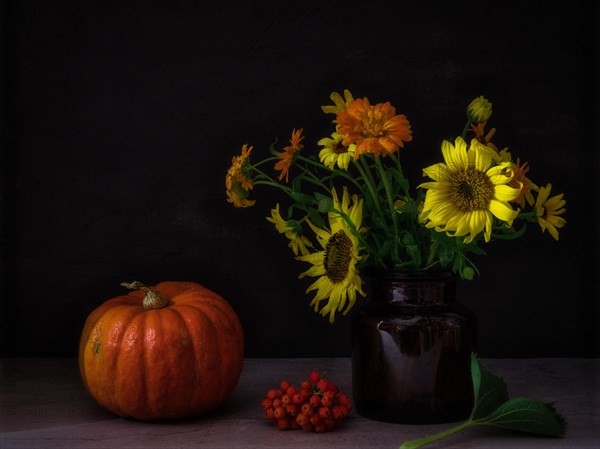 Still life with pumpkin next to rowan berries and autumn flowers in glass