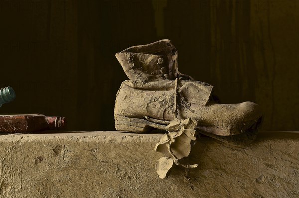 Work shoe on wall with lump of clay on lace and 2 liquor bottles