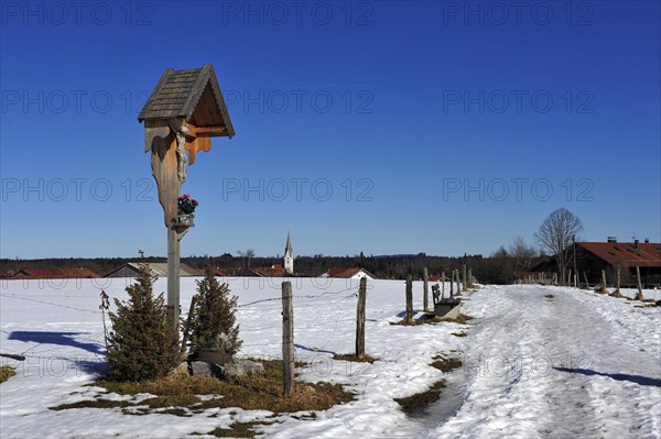 Wooden shrine in snowy landscape with crucifix and flowerpot