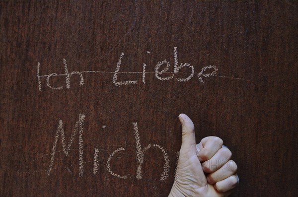 Hand with thumb up in front of metal wall with inscription I love myself