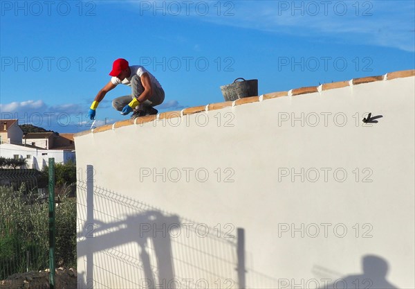 Bricklayer squats on house roof and grouts the roof tiles