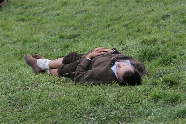 Young man in Bavarian traditional costume sleeps off intoxication from Oktoberfest on lawn