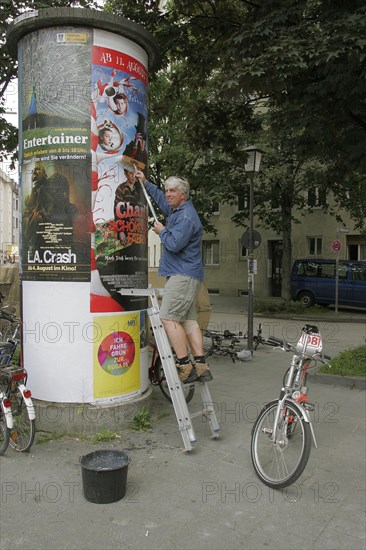 Man on ladder sticking poster on advertising pillar