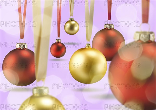 Some golden and red Christmas balls on ribbon floating over pink ground with bright light spots