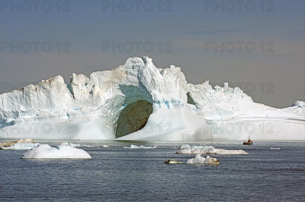 Small fishing boat in front of huge iceberg with two large caves