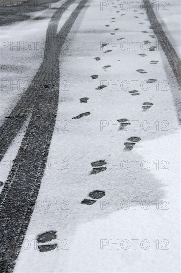 Traces of car tyres and footprints on thin snow cover of asphalt road