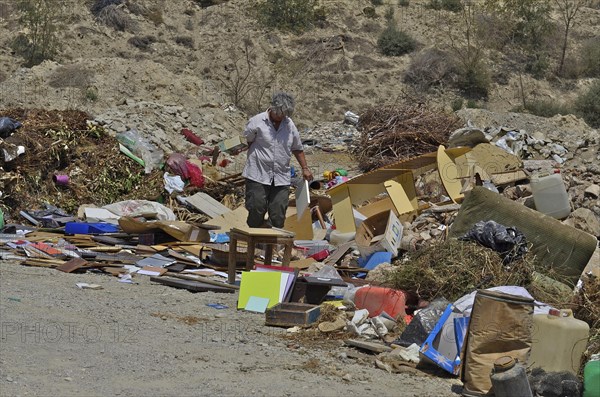 Old woman looking for useful things in rubbish heap