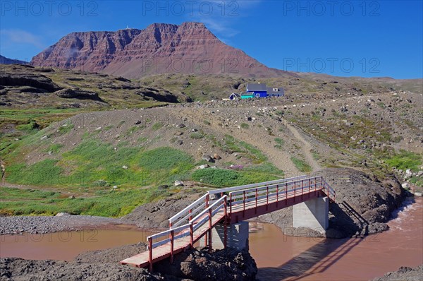 Reddish brown river flowing through a green arctic landscape