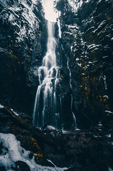 The Burgbach waterfall with snow in winter. Waterfall with stone steps in Schapbach