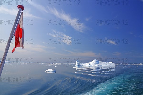 Greenlandic flag and icebergs in the calm waters of Disko Bay