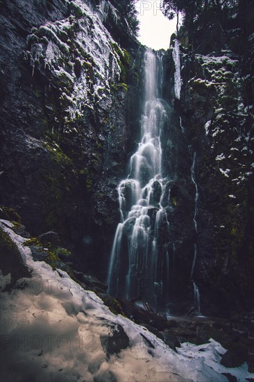 The Burgbach waterfall with snow in winter. Waterfall with stone steps in Schapbach