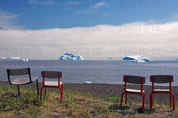 Chairs standing in front of a bay with icebergs floating in it