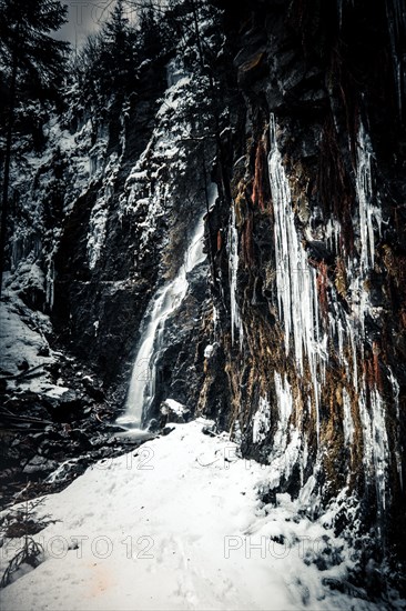 The Burgbach waterfall with snow in winter. Waterfall with stone steps in Schapbach