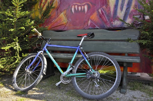 Bicycle leaning against green bench with vampire teeth in the background at Oktoberfest