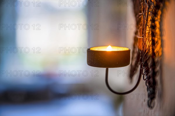 Burning candle as wall light in the backlight of a window