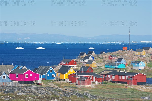 Different coloured wooden houses in front of the bay with icebergs