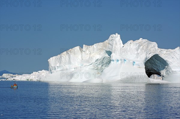 Small fishing boat in front of huge iceberg with two large caves