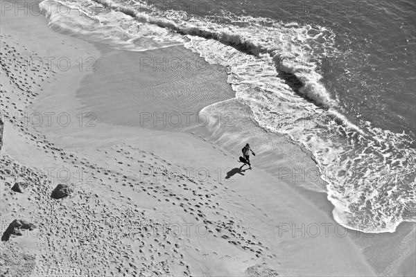 Man with guitar on lonely beach with footprints in sand