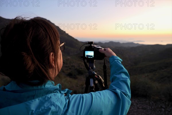 Woman taking pictures on tripod at sunrise by the sea