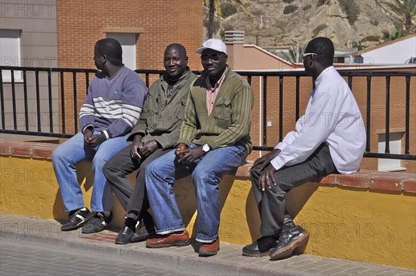 African men sitting on the wall of a garden fence