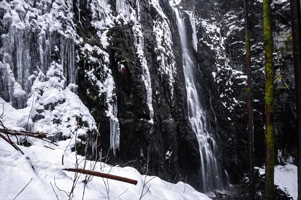 The Burgbach waterfall with snow in winter. Waterfall with stone steps in Schapbach