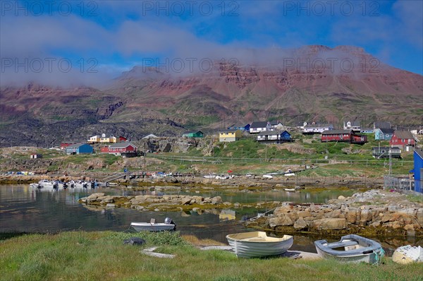 Small boats lie in front of houses and red volcanic mountains