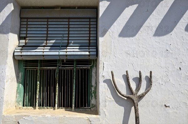 Pitchfork leaning against house wall next to barred window