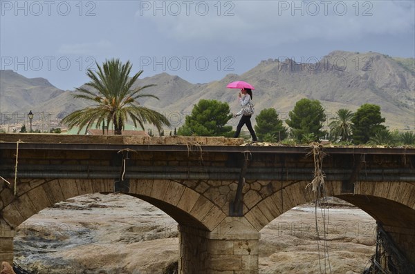 Woman with umbrella runs over bridge with bridge railing torn away after flood