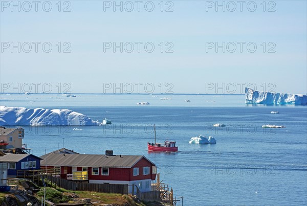 Dwellings and fishing boat at the edge of a bay covered with icebergs