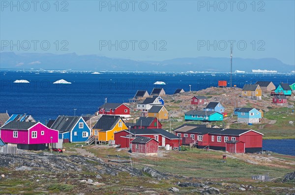 Different coloured wooden houses in front of the bay with icebergs