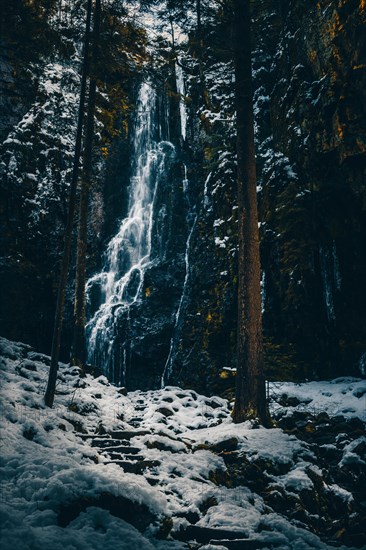 The Burgbach waterfall with snow in winter. Waterfall with stone steps in Schapbach