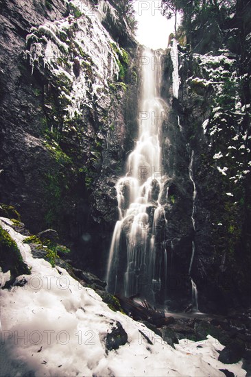 The Burgbach waterfall with snow in winter. Waterfall with stone steps in Schapbach