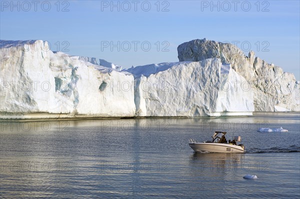 Huge icebergs and a small boat in the glow of the midnight sun