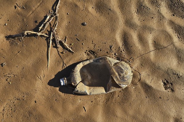 Washed up crushed plastic bottle on clay soil