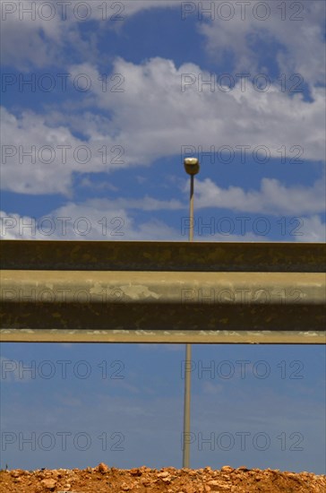 Guard rail from behind with street lamp and cloudy blue sky