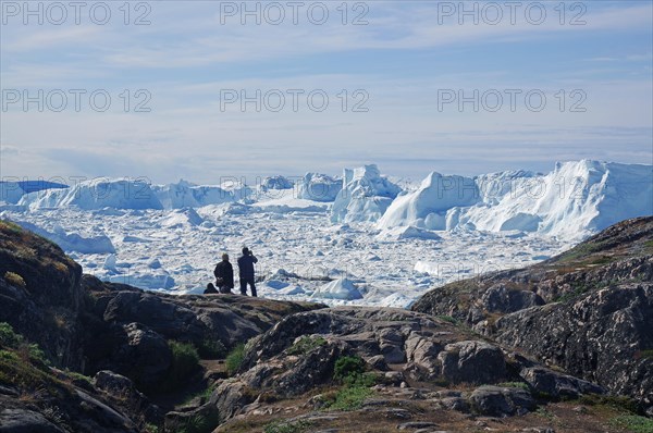 People sitting in front of fjord covered with ice and icebergs