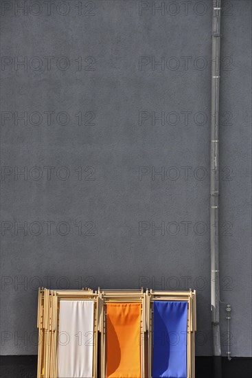 Grey wall with downpipe from gutter and coloured deck chairs in park