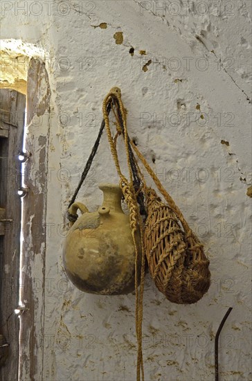 Clay drinking vessel with bag of esparto grass on nail in front of white wall