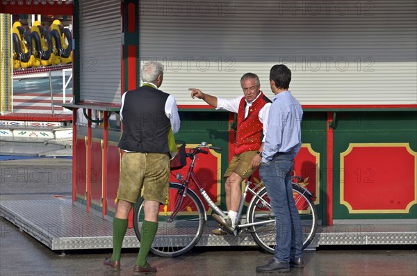 Men in lederhosen chatting with showman at deserted Oktoberfest in front of it begins