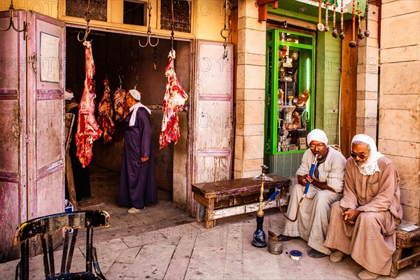 Men smoking water pipes in front of a butcher's shop