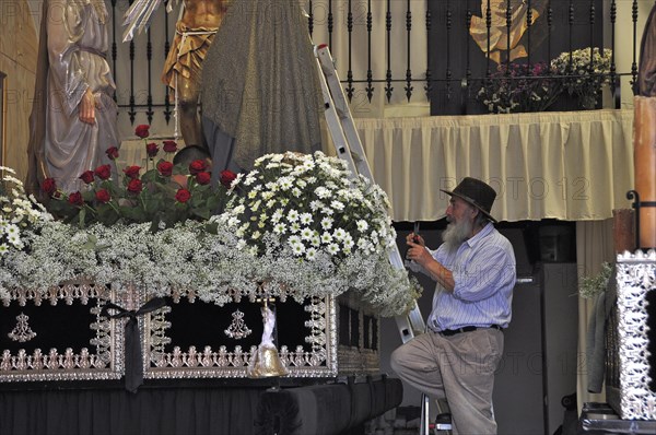 Old man with hat decorates altar in church for Easter procession