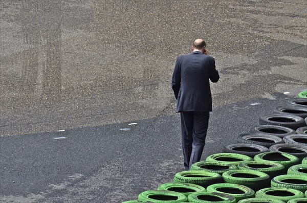 Man with mobile phone to ear in front of stacked car tyres at racecourse