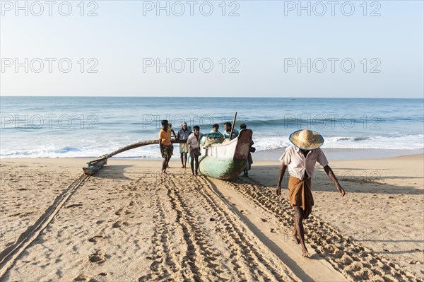 Fishermen pull fishing boat out of the sea onto the sandy beach